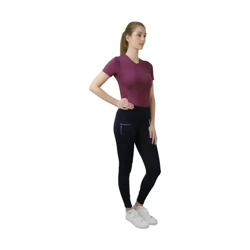 A woman wearing a maroon hy equestrian synergy t-shirt paired with black leggings featuring a zip thigh pocket