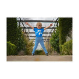 A cheerful boy wearing bright blue pull-on tots jodhpurs from hy equestrian zeddy tots stands outdoors joyfully