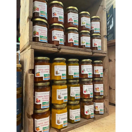 Glass jars of kay’s homemade gluten free chutney in various colors including spicy apricot on wooden shelves