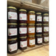 Rows of colorful glass jars of kay’s homemade jams from north devon with gold lids and fruit-labeled tags including quince jelly
