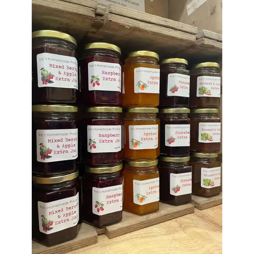 Rows of colorful glass jars of kay’s homemade jams from north devon with gold lids and fruit-labeled tags including quince jelly