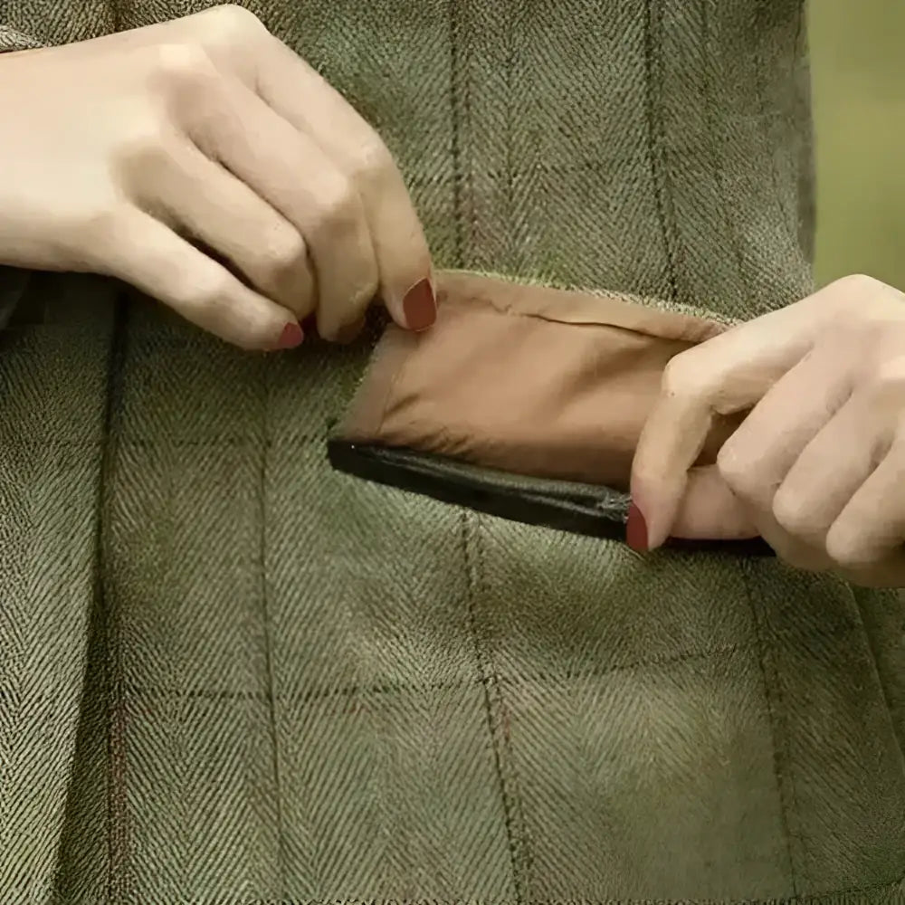 A brown leather zipper pouch being pulled from the pocket of a ladies launton deluxe tweed riding jacket