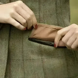 A brown leather zipper pouch being pulled from the pocket of a ladies launton deluxe tweed riding jacket