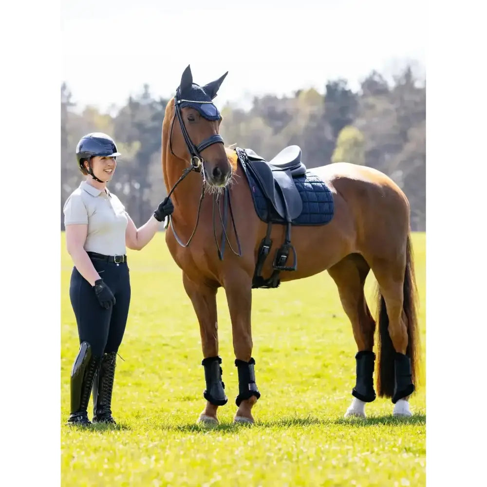 A chestnut horse wearing a navy lemieux 3d mesh dressage square designed for maximum airflow in an open field