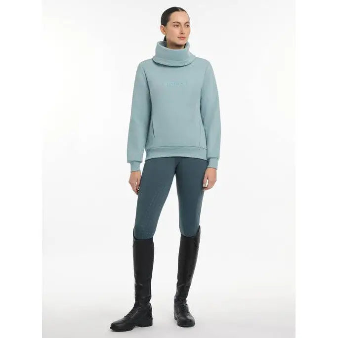 Woman in Lemieux Adele Funnel Neck Sweat Glacier, gray leggings, and tall black boots