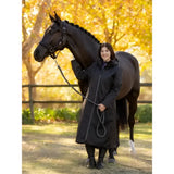 Woman wearing lemieux all elements robe black riding coat with hood and front zipper standing beside a horse