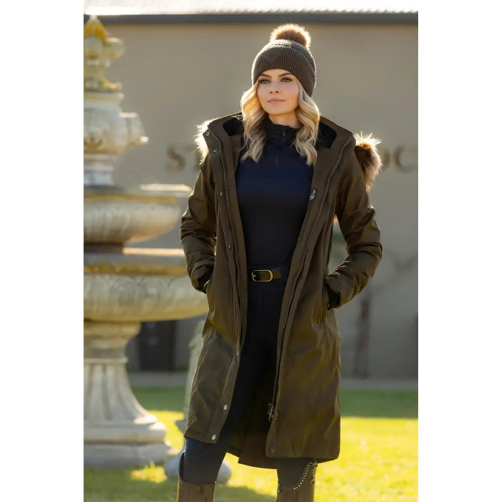 Woman in long olive green Lemieux Anya Waterproof Riding Coat Alpine and knit hat