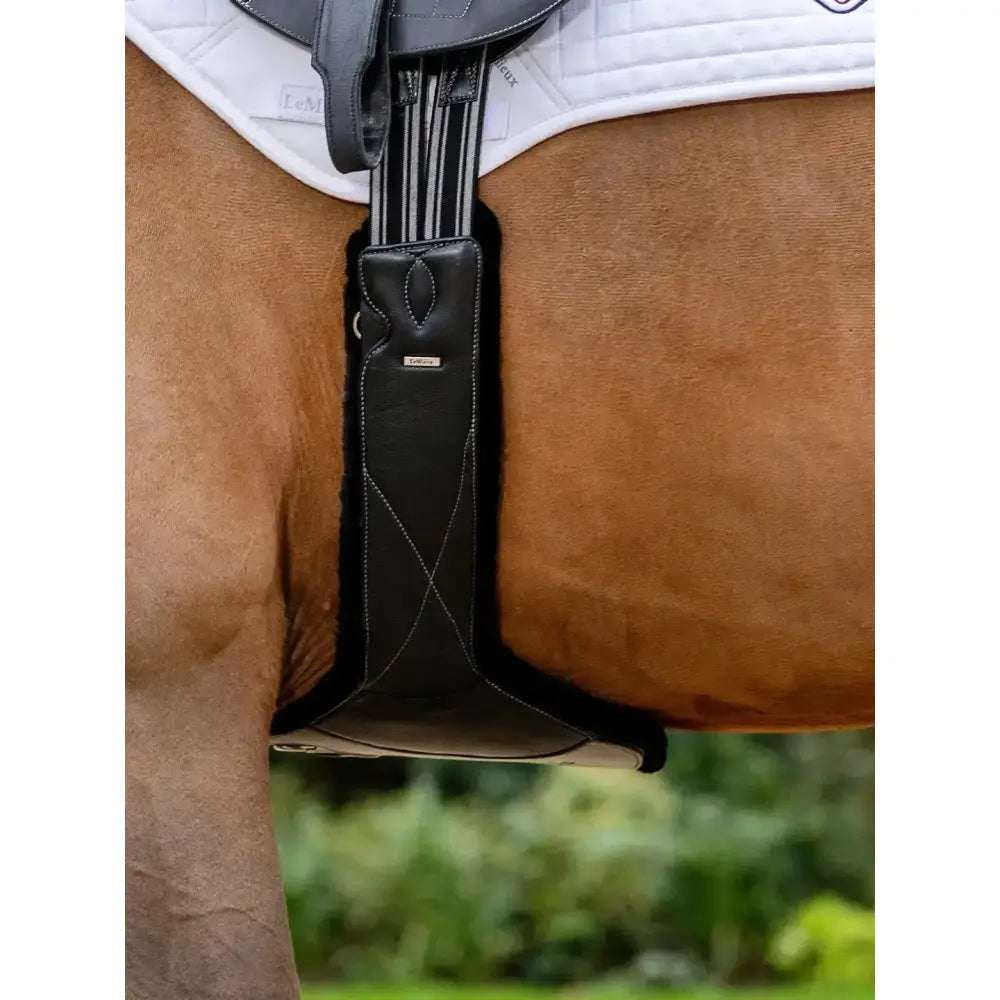 Black leather saddle pad with white stitching and small silver logo for lemieux arika simuwool contoured long stud girth