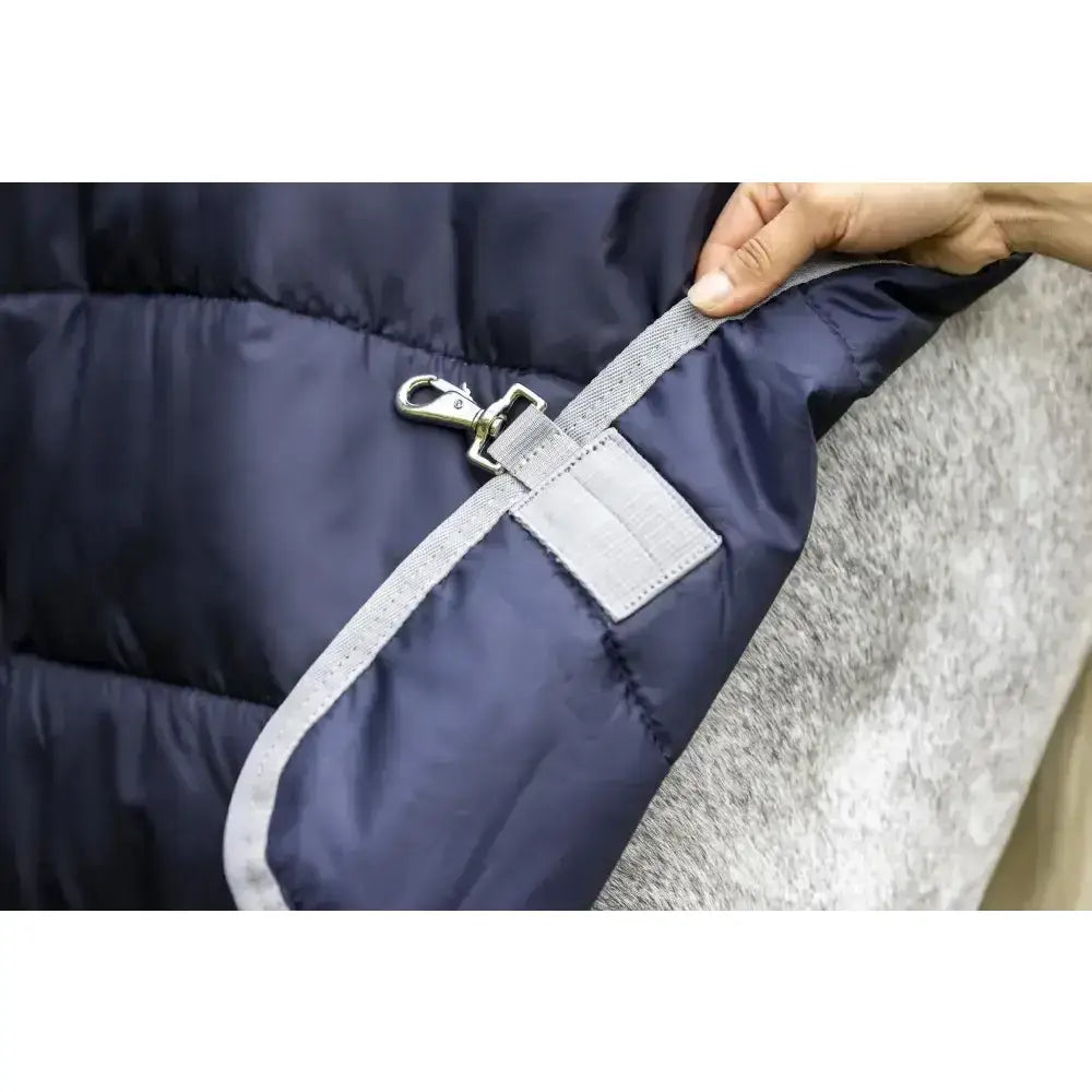 Navy blue quilted lemieux arika storm-tek puffer jacket with gray webbing strap and metal hook clasp close-up