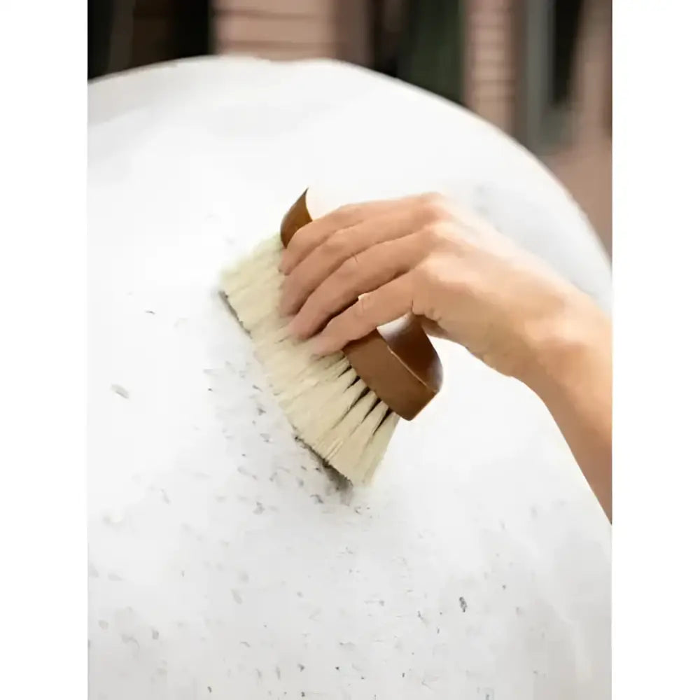 A hand holding the lemieux artisan deep clean dandy brush brown with natural bristles brushing white foam off a horse