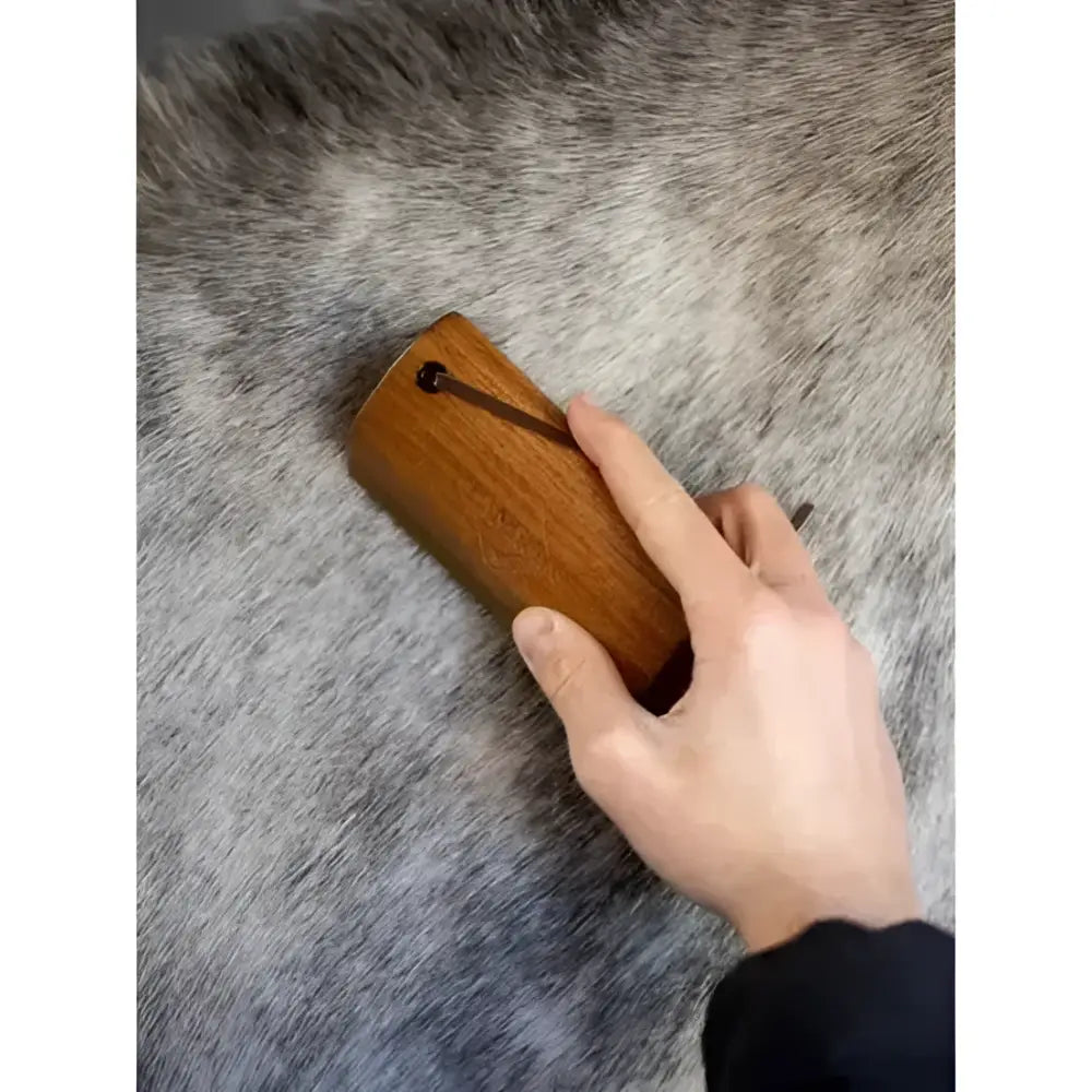 A hand holds a lemieux artisan shedding comb brown with wooden teeth and a dark metal handle for grooming