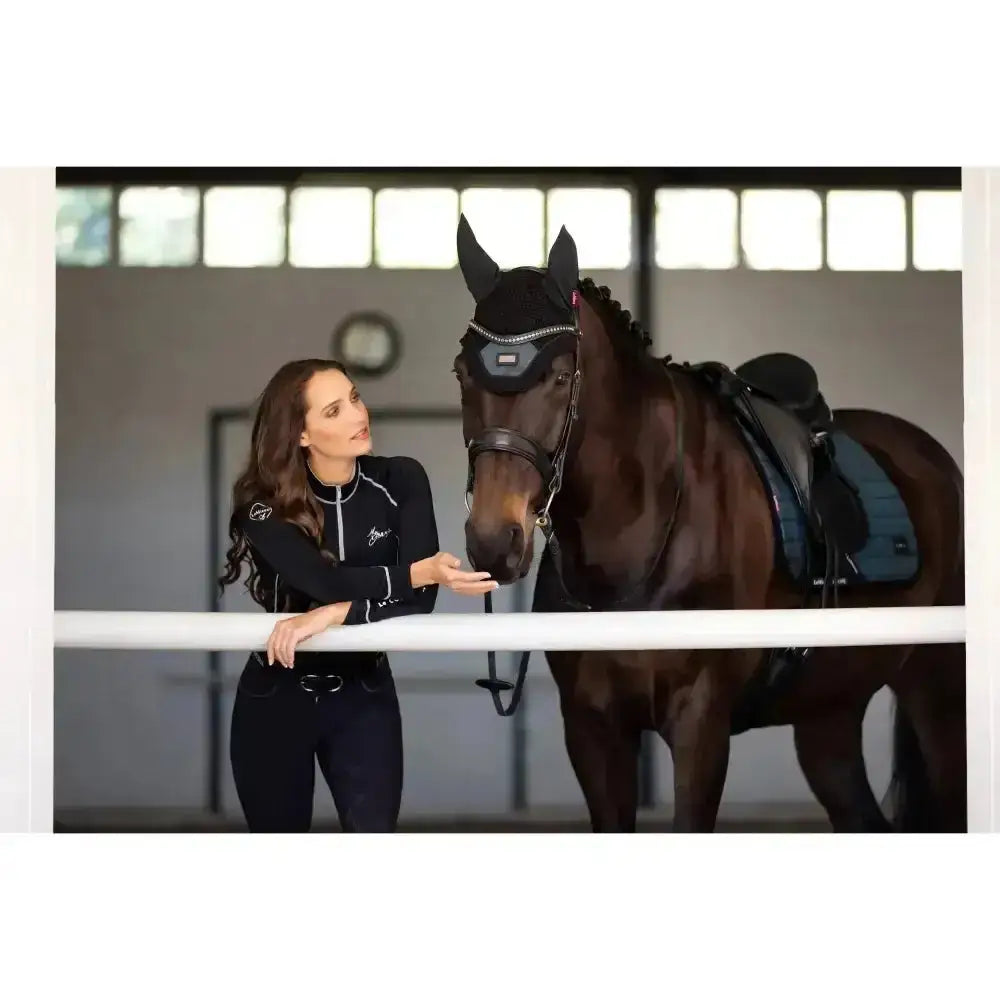 Dark brown horse wearing black lemieux base layer head covering with silver studs and dark blue saddle for riding apparel