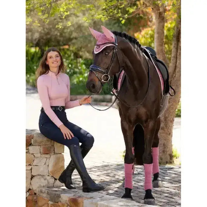 A dark brown horse wearing a pink lemieux base layer blossom bridle and matching pink leg wraps for riding gear