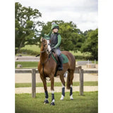 A young rider wearing lemieux base layers hunter green sits on a brown horse with matching protective leg wraps