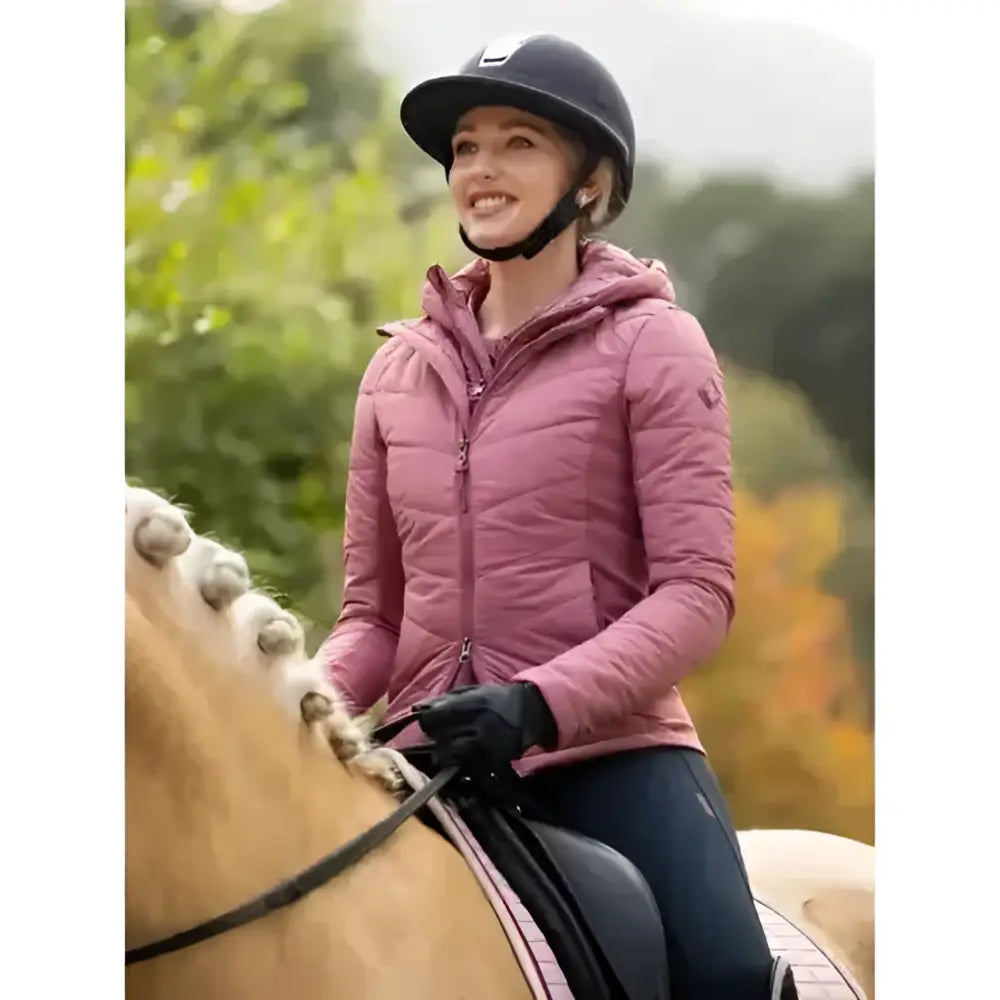 A pink quilted lemieux brioney hybrid jacket peony with a hood and front zipper worn by a rider