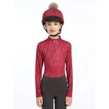 A young girl wears a vibrant red lemieux casey hat silk ember riding helmet with a fluffy pom-pom and black trim