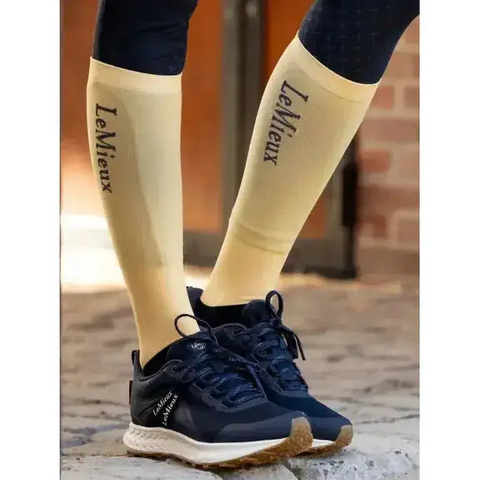 Cream-colored lemieux competition socks with black branding worn over dark leggings and navy athletic shoes