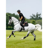 A sleek white horse wearing a lemieux cotton contact square black saddle pad with black protective leg wraps