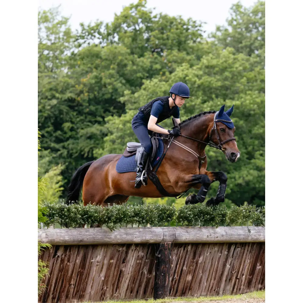 A chestnut horse jumping wearing lemieux cotton close contact saddle pad navy with black leg wraps