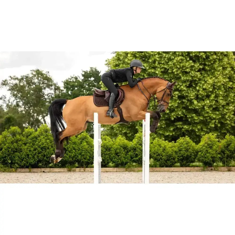 A chestnut horse jumping wearing a lemieux crystal suede close contact square saddle in brown forward-cut style
