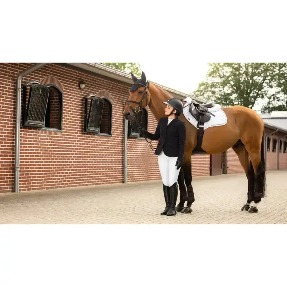 A brown horse with a black bridle stands beside a rider wearing lemieux crystal suede close white saddle pad