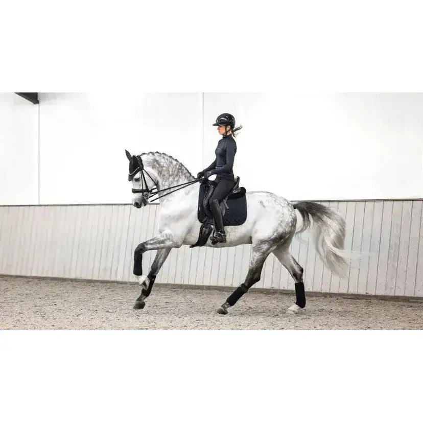 A sleek dapple-gray horse with black lemieux crystal suede dressage saddle and leather girth protection wraps