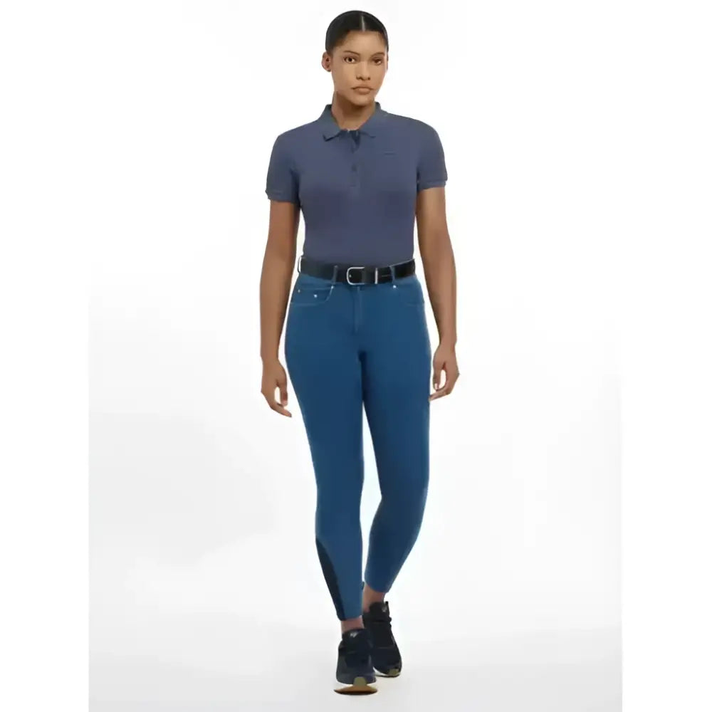 A model wears lemieux dolly denim breech riding pants in deep teal with black side panels paired with a navy polo shirt