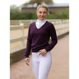A woman wearing a deep purple v-neck sweater over a white shirt modeling lemieux drytex waterproof breeches with waterproof rating