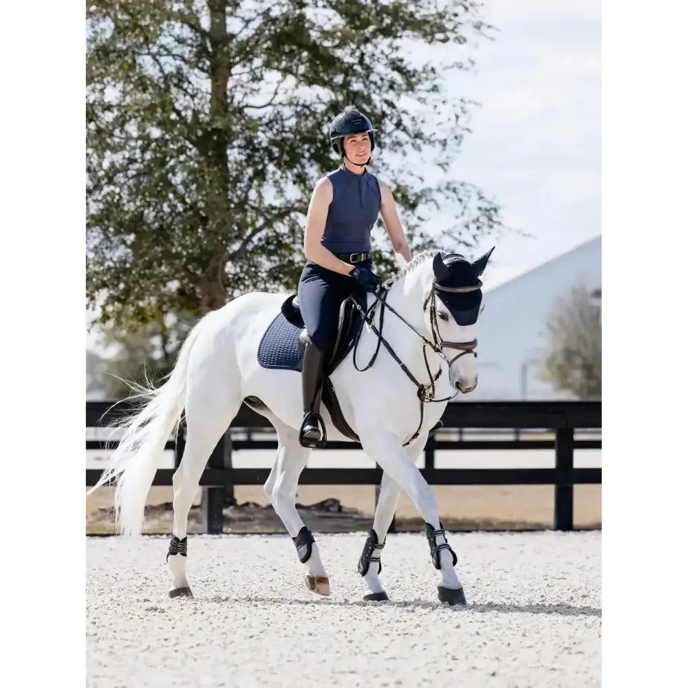 A white horse wearing black protective gear and a lemieux finesse eurojump faux leather eurojump square navy saddle pad