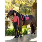 A dark brown horse wearing lemieux grafter brushing boots cranberry pink hoof boots and matching saddle pad and headpiece