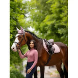 A brown horse with a white blaze wearing a pink mesh lemieux halle lightweight base layer peony and black bridle