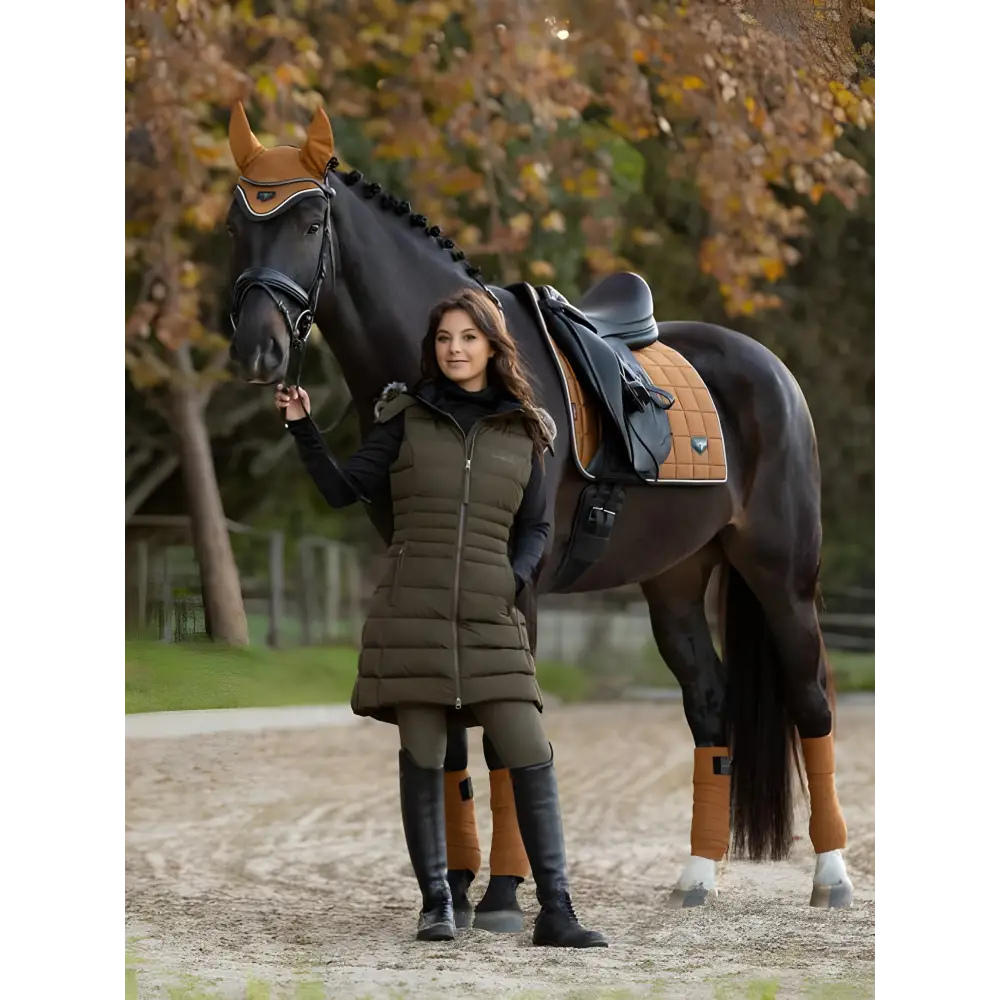 Dark horse with saddle beside person wearing Harper Longline Puffer Gilet Alpine