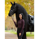 A sleek black friesian horse with a glossy coat stands beside a rider wearing lemieux heyden lightweight base layer in damson colour