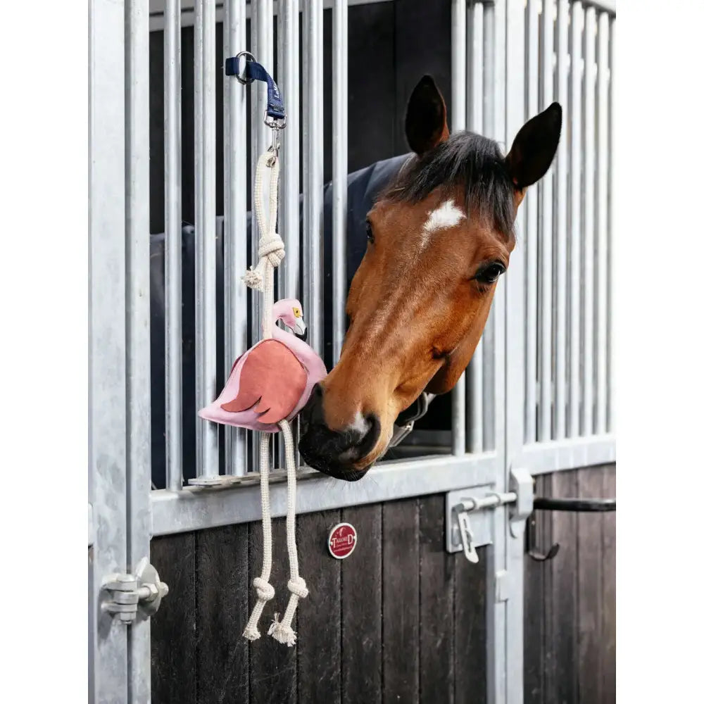 Pink lemieux horse toy flamingo with rope handles and blue strap hanging from stable bars for horse play