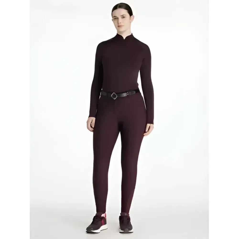 A sleek maroon long sleeve top with high neckline and subtle seams paired with lemieux isabelle seat breeches for equestrian use