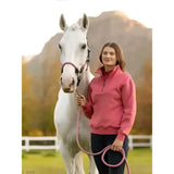 A woman stands beside a white horse wearing a lemieux keira quarter zip sweat cranberry pink fleece pullover holding the lead rope
