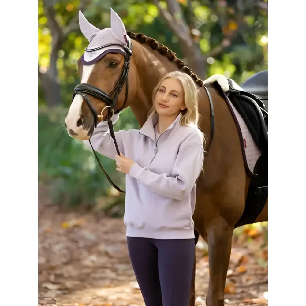 A horse wears a white mesh ear cover with purple trim while sporting the lemieux keira quarter zip sweat lilac