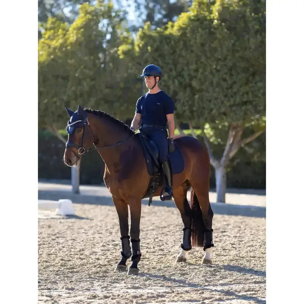 A dark brown horse stands in an outdoor arena wearing a lemieux le cool navy dressage pad with cool grip features
