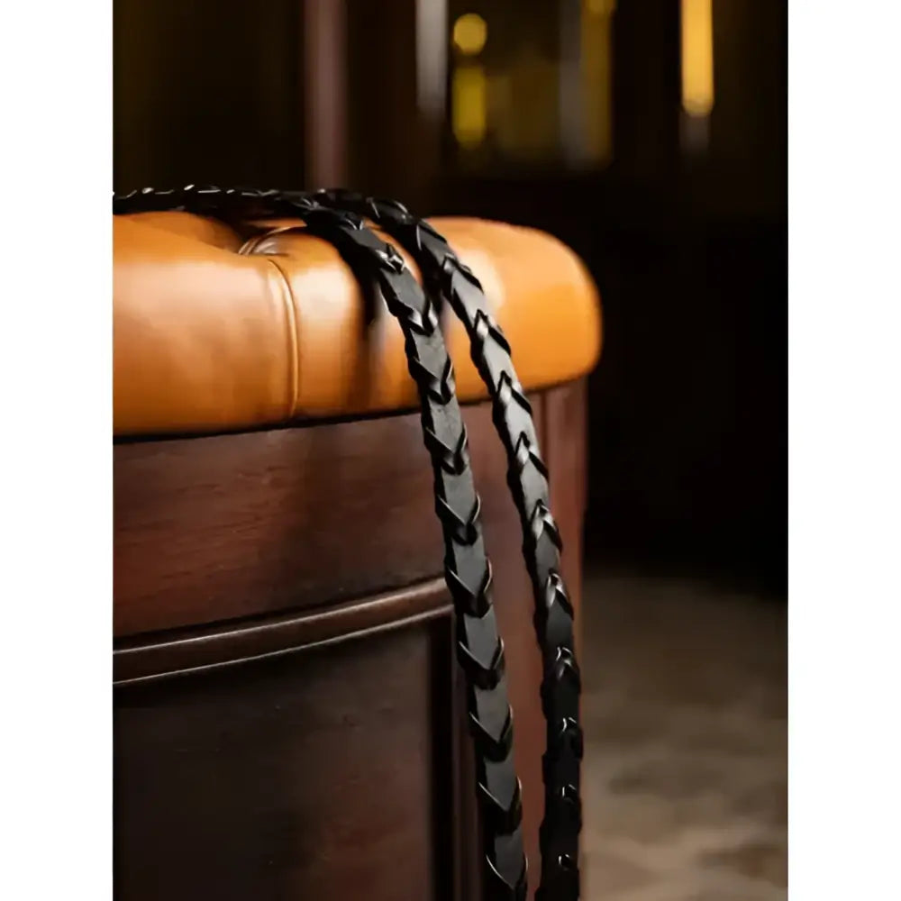 Black lemieux leather laced classic leather reins resting on a tan tufted ottoman showing braided leather strap