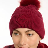A maroon knitted lemieux lila beanie ember with a fluffy pom-pom and diamond-shaped embroidered patch