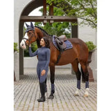 A woman in a sleek navy blue lemieux loire classic close riding outfit stands beside a brown horse with white markings