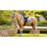 A palomino horse wearing a light blue lemieux loire classic quilted dressage square aqua saddle pad with black straps and matching bridle
