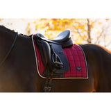 Red quilted lemieux loire classic dressage square ember saddle pad with white trim and black leather saddle on top
