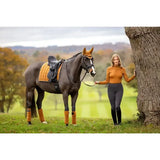 Dark brown horse wearing a lemieux loire classic dressage square ginger saddle pad and matching orange leg wraps