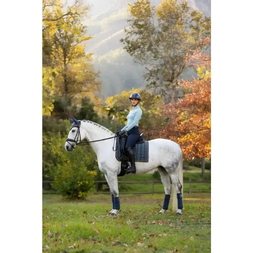 A white horse with gray dapples wearing lemieux loire classic dressage square petrol with dark blue leg wraps