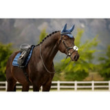 A dark brown horse wearing a blue padded saddle pad and matching lemieux loire fly hood atlantic ear bonnet