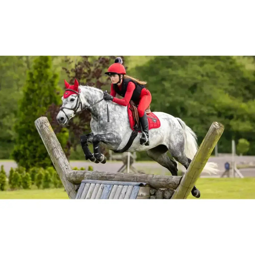 A white dapple horse jumping with a red lemiuex loire range saddle pad made of woven satin fabric