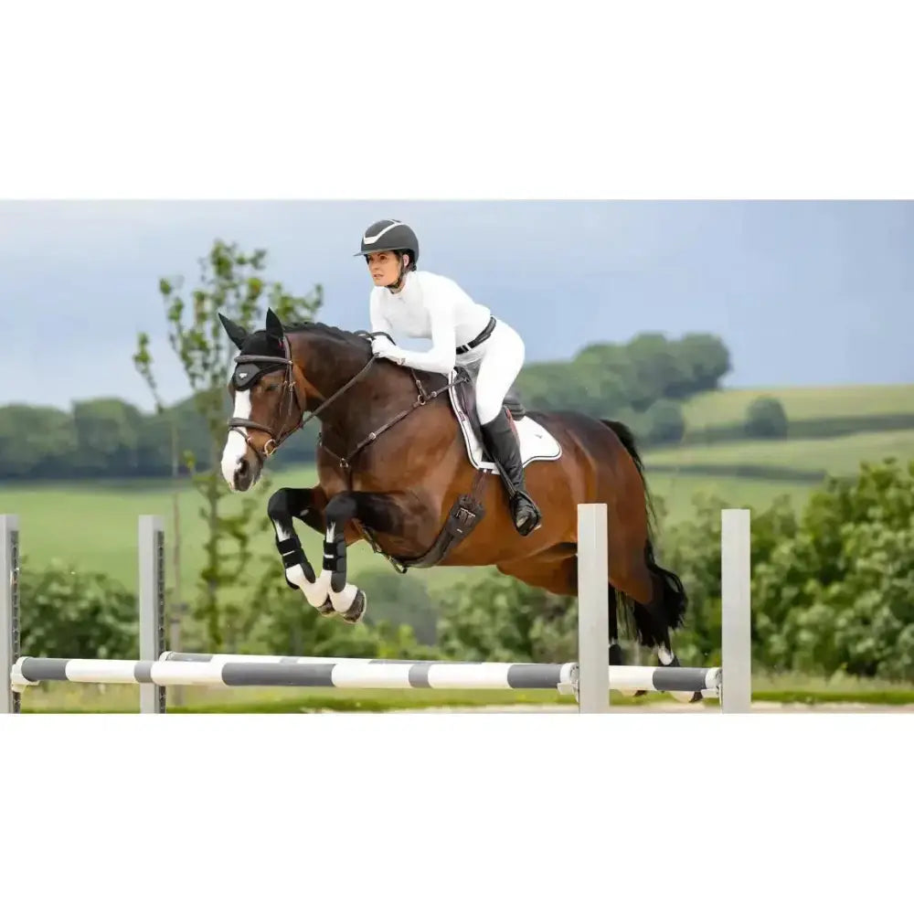 Brown horse wearing lemieux loire gp square white saddle pad with bridle and saddle in riding setting