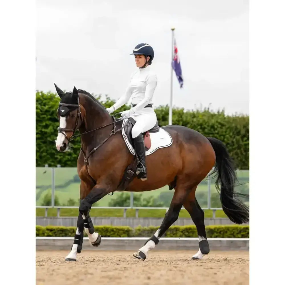 A sleek dark brown horse wearing a white lemieux loire gp square saddle pad and riding gear