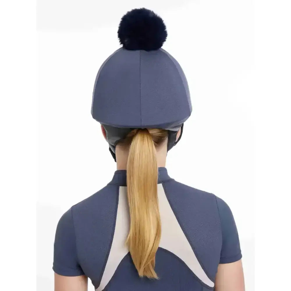 A navy blue lemieux maria mesh equestrian helmet with a black fluffy pom-pom on top in silk dusk blue